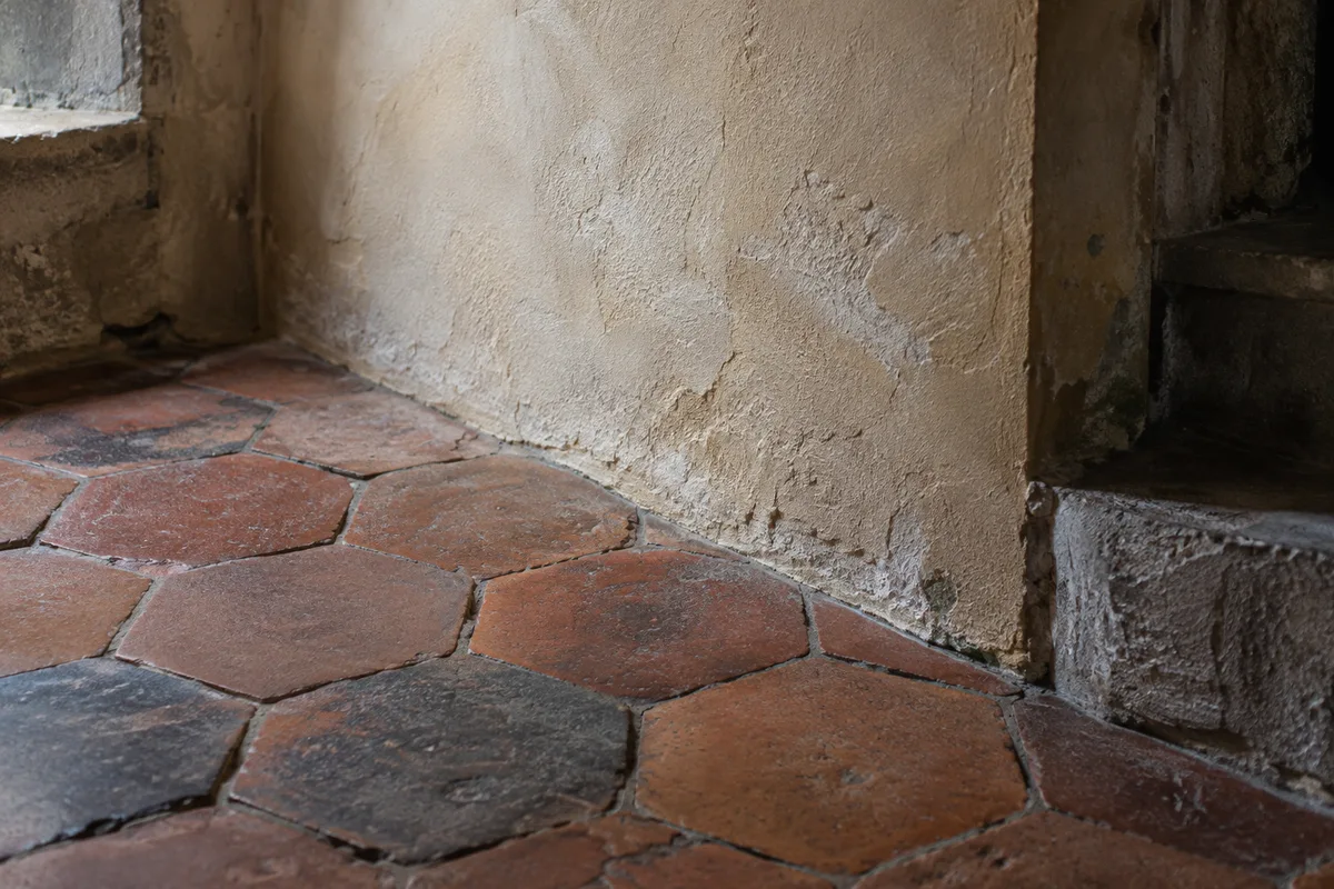 Mur enduit à la chaux de teinte ocre clair et sol en tomettes anciennes dans une maison de caractère