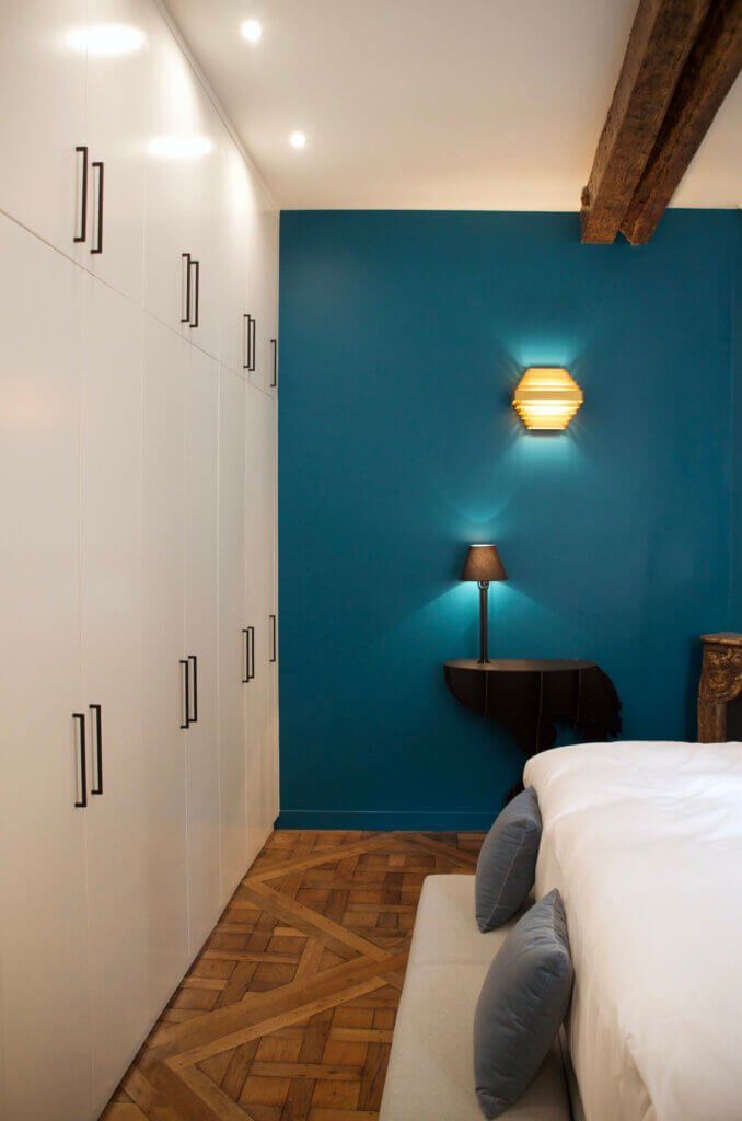 Bedroom with bespoke wardrobes, blue accent wall and parquet flooring